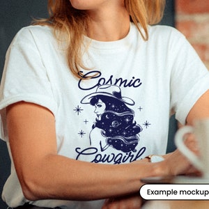 May include: White t-shirt with a blue graphic of a woman wearing a cowboy hat with stars and the text "Cosmic Cowgirl".