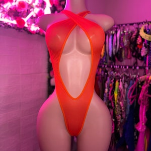 Op de afbeelding: Een feloranje bodysuit met een hoog uitgesneden beenontwerp, een diepe centrale uitsnijding en een halterhalslijn met gekruiste bandjes over de borst. Het kledingstuk is gemaakt van een doorschijnende, lichtgewicht stof met afgewerkte randen.