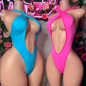 Puede incluir: Dos ba&ntilde;adores de una pieza sobre maniqu&iacute;es. Uno es de color azul cian brillante y el otro es de color rosa intenso. Ambos presentan un dise&ntilde;o de pierna alta, un escote muy pronunciado y tirantes finos que se cruzan sobre el pecho.