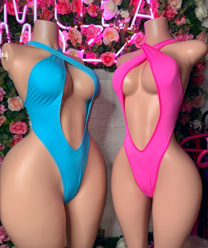 Puede incluir: Dos ba&ntilde;adores de una pieza sobre maniqu&iacute;es. Uno es de color azul cian brillante y el otro es de color rosa intenso. Ambos presentan un dise&ntilde;o de pierna alta, un escote muy pronunciado y tirantes finos que se cruzan sobre el pecho.