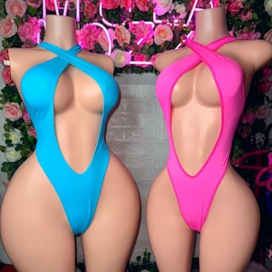 Puede incluir: Dos bodys sin mangas exhibidos en maniqu&iacute;es, uno en azul cian brillante y el otro en rosa intenso. Cada prenda presenta un dise&ntilde;o de pierna alta, un escote profundo y un detalle de tiras cruzadas tipo halter en el pecho.