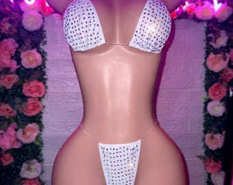 Può includere: Completo bikini bianco con spalline trasparenti e strass. La parte superiore è di stile triangolare e la parte inferiore è di stile tanga.