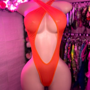 Op de afbeelding: Een feloranje bodysuit met een halterhalslijn met gekruiste bandjes op de borst, een diepe uitsnijding die doorloopt tot aan de taille en een hoog uitgesneden beenontwerp. Het kledingstuk is gemaakt van een doorschijnende, fijne mesh-stof.
