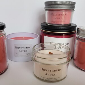 May include: Five glass jars with lids containing red and pink scented candles. The candles are labeled "Honeycrisp Apple" and are hand-poured soy candles.