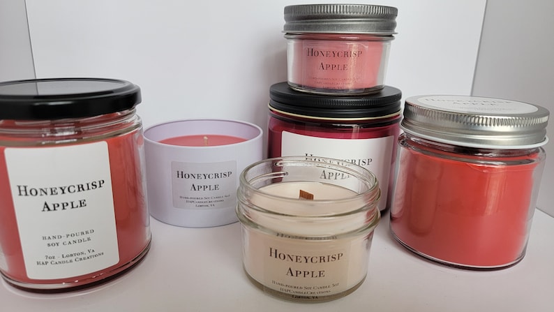 May include: Five glass jars with lids containing red and pink scented candles. The candles are labeled "Honeycrisp Apple" and are hand-poured soy candles.