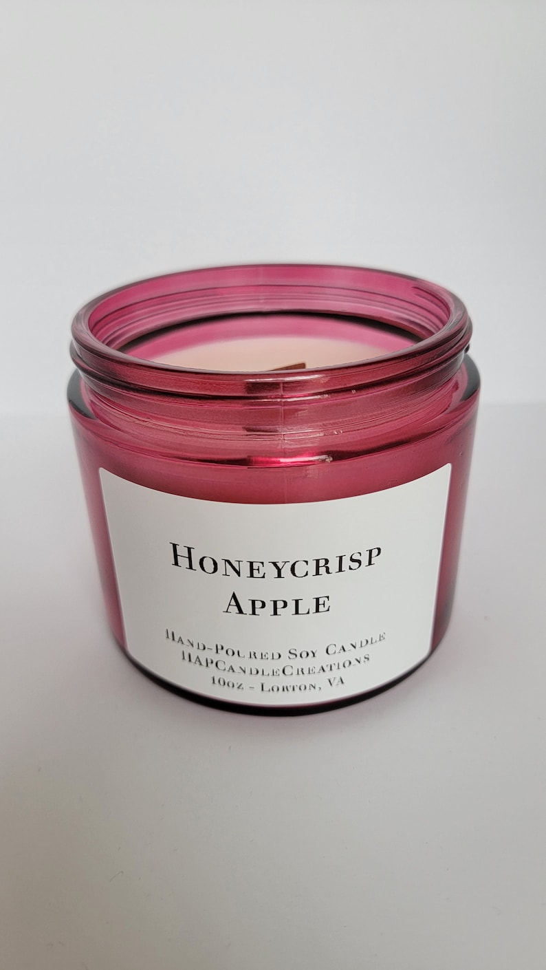 May include: A red glass jar candle with a white label that reads "Honeycrisp Apple" and "Hand-Poured Soy Candle Happy Candle Creations 10oz - Lorton, VA".