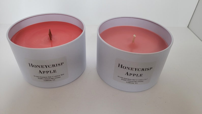 May include: Two white candle jars with pink wax and wooden wicks. The labels read "Honeycrisp Apple" and are handmade soy candles.