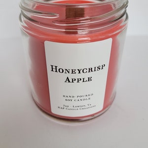 May include: A clear glass jar candle with a red soy wax scent labeled "Honeycrisp Apple". The label also states "Hand-poured Soy Candle" and "7oz - Lorton, VA. Hap Candle Creations."