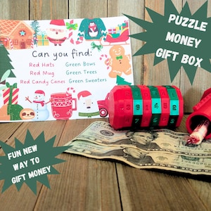 May include: A red and green puzzle money gift box with a Christmas theme. The box has a combination lock and a slot to insert money. The box is open and there is a dollar bill inside. The image also includes a card with the text "Can you find: Red Hats, Green Bows, Red Mug, Green Trees, Red Candy Canes, Green Sweaters".