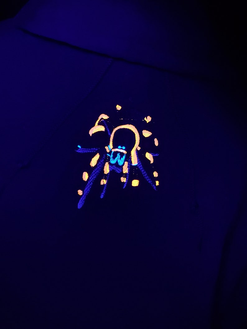 May include: A black hoodie with a yellow and blue spider design on the front. The spider is outlined in yellow and has a blue body.