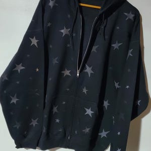 May include: Black zip-up hoodie with a star pattern. The stars are a darker shade of gray than the black fabric.