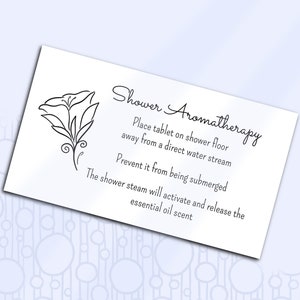 Könnte beinhalten: Eine weiße Karte mit schwarzem Text und einer einfachen Strichzeichnung einer Blume. Der Text lautet "Shower Aromatherapy", "Place tablet on shower floor away from a direct water stream", "Prevent it from being submerged", and "The shower steam will activate and release the essential oil scent."