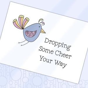 Pode incluir: Um cartão branco com uma ilustração de um pássaro de desenho animado. O pássaro é azul claro com uma cauda rosa, amarela e verde. O texto no cartão diz "Dropping Some Cheer Your Way".