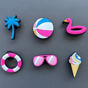 May include: A collection of colorful beach-themed charms. Includes a blue palm tree, a beach ball with pink and white stripes, a pink flamingo float, a pink and white life preserver, pink sunglasses, and an ice cream cone.