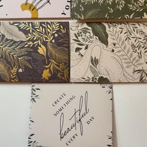 May include: A collection of decorative rectangular cards with various designs. Some cards feature animal and botanical patterns in shades of red, green, and gold. Other cards have inspirational text, including "Today is Yours" and "Create Something Beautiful Every Day."