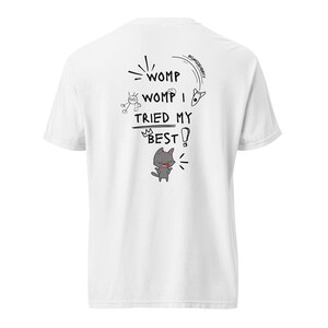 May include: White t-shirt featuring a cartoon design on the back. The design includes the text "WOMP WOMP I TRIED MY BEST!" and a drawing of a grey cat, plus other playful illustrations.