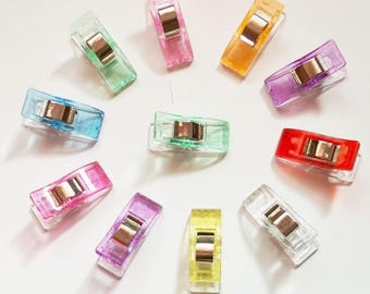 May include: Assortment of ten colorful plastic clips with silver metal spring closures. The clips are in various colors including red, orange, yellow, green, blue, purple, and clear.