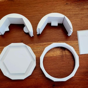 May include: White 3D-printed components, including two curved pieces, a hexagonal base, a ring, and a rectangular piece with text. The items are arranged on a wooden surface. The text on the rectangular piece is "GOWIK".