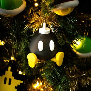 Puede incluir: Un adorno navideño negro y blanco con forma de bomba con pies amarillos. El adorno está colgado de un árbol de Navidad verde con serpentinas doradas.