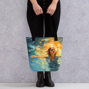 May include: A tote bag featuring a painting of a woman swimming underwater with sunlight shining down on her. The woman is wearing a white swimsuit and has long brown hair. The water is a vibrant blue and green with sparkling light.
