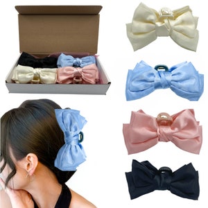 May include: Set of five satin hair clips in various colors, including black, white, pink, blue, and light blue. Each clip features a large bow with a decorative clasp.