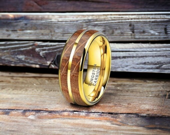 May include: A gold tungsten carbide ring with a brown wood inlay. The ring is engraved with the words "Tungsten Carbide".