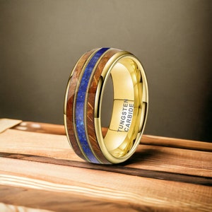 May include: A gold tungsten carbide ring with a brown wood inlay and blue lapis lazuli accents. The ring is engraved with "TUNGSTEN CARBIDE".
