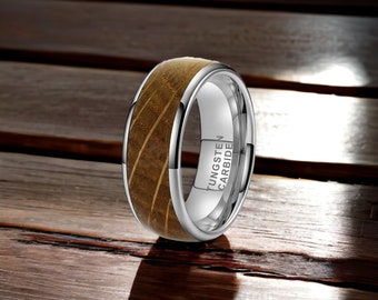 May include: A silver tungsten carbide ring with a brown wood inlay. The ring is engraved with the words "Tungsten Carbide".