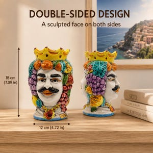 Puede incluir: Dos jarrones de cerámica con forma de cabeza y diseño de doble cara con un rostro esculpido en ambos lados. Los jarrones están decorados con una corona amarilla, uvas moradas y detalles en naranja. Miden 18 cm de alto y 12 cm de ancho.