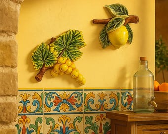 May include: Decorative wall art featuring a lemon and a bunch of grapes, each with green leaves and brown stems. The art is set against a yellow wall, with colorful patterned tiles below. A glass bottle and wooden cabinet are also visible.