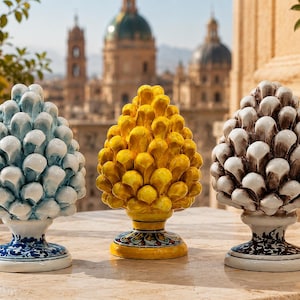 Puede incluir: Tres esculturas de cerámica con forma de piña dispuestas en fila. La escultura de la izquierda es azul claro, la del centro es amarillo brillante y la de la derecha es blanca con sombreado marrón oscuro. Cada pieza presenta un patrón de escamas.