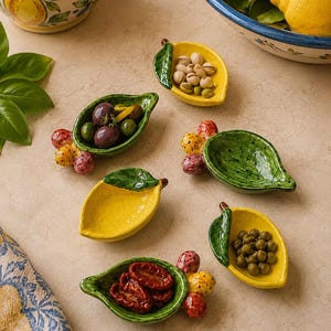 Könnte beinhalten: Ein Set aus sechs zitronenförmigen Keramikschalen, die jeweils mit einem grünen Blatt und kleinen bunten, fruchtartigen Verzierungen versehen sind. Die Schalen sind gelb und grün bemalt und enthalten teilweise Oliven, Pistazien, Erbsen oder getrocknete Tomaten.
