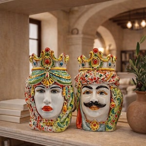 Könnte beinhalten: Zwei Keramik-Kopfvasen mit kunstvollen, handbemalten Details. Eine zeigt eine Figur mit Krone, grünem Kopfschmuck und roten Lippen. Die andere zeigt eine Figur mit Krone, gemustertem Turban und einem dunklen Schnurrbart. Beide haben farbenfrohe, florale Muster.