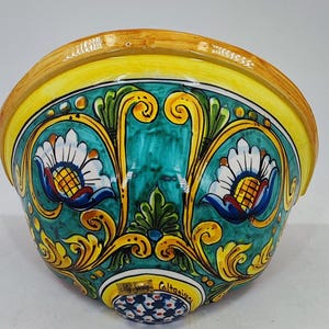 May include: A ceramic wall pocket with a vibrant, hand-painted design. The bowl features a yellow rim, teal interior, and ornate floral patterns in yellow, white, and blue. The base has a decorative pattern and text that reads "My Sicily Caltagirone."