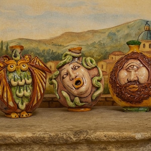May include: Three decorative ceramic vases with unique designs. The first is an owl, the second a face with snakes, and the third a bearded face. The vases are in shades of brown, green, and yellow, and are displayed on a stone surface.