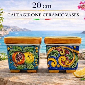Puede incluir: Dos jarrones de cerámica de Caltagirone, cada uno de 20 cm de altura, con forma cuadrada y un diseño vibrante. Los jarrones presentan un fondo azul con motivos florales y frutales coloridos, incluyendo granadas y limones. La parte superior y los pies son de color marrón dorado.
