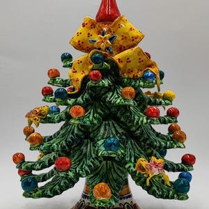 Pode incluir: Uma árvore de Natal de cerâmica com uma ponta vermelha, laço amarelo e ornamentos coloridos. A árvore é verde com uma base decorativa e é adornada com ornamentos vermelhos, azuis e laranja. A base tem o texto "My Sicily Caltagirone".