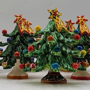 Könnte beinhalten: Sechs keramische Weihnachtsbäume. Jeder Baum ist grün mit bunten Kugeln und einer Sternspitze. Die Bäume haben ein handgemaltes Aussehen und stehen auf einem hellen Sockel. Festliche Dekorationen.