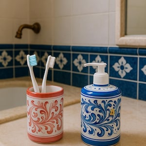 Puede incluir: Un conjunto de baño en una encimera, que incluye un porta cepillos de dientes y un dispensador de jabón. El porta cepillos es rojo y blanco con un diseño floral, con dos cepillos de dientes. El dispensador de jabón es azul y blanco con un patrón floral.