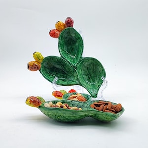 Peut inclure: Un plat de service en céramique vert en forme de figuier de Barbarie avec trois sections. Le plat est rempli de noix et d'amandes.