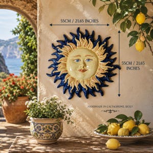 Könnte beinhalten: Eine keramische Sonnen-Wandplatte mit einem cremefarbenen Gesicht, blauen Augen und roten Lippen, umgeben von gelben und dunkelblauen Strahlen. Das Stück misst 55 cm in der Breite und 55 cm in der Höhe und ist handgefertigt in Caltagirone, Sizilien.