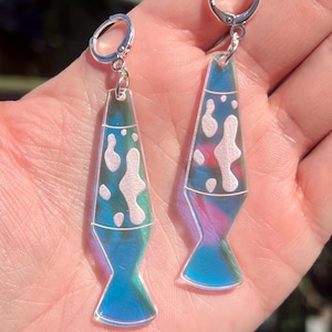 Op de afbeelding: Een paar iriserende lava lamp oorbellen. De oorbellen hebben een heldere, druppelvorm met een blauw-roze verloop en witte blob-ontwerpen. De oorbellen hangen aan zilveren hoepels.