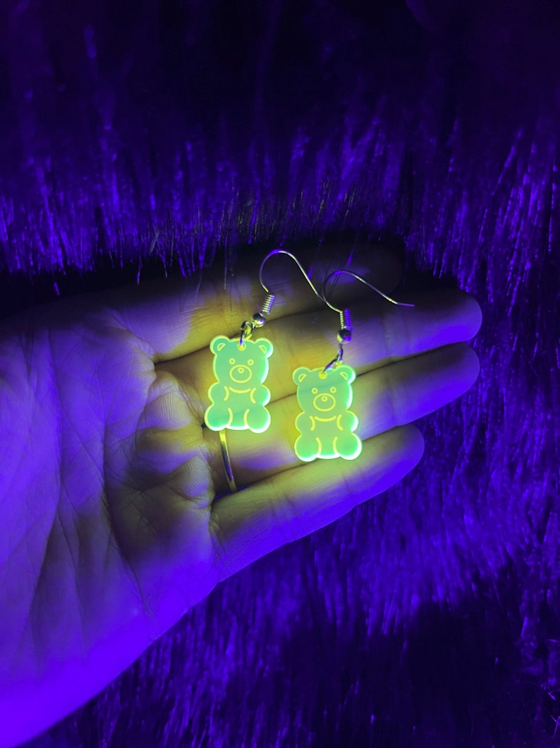 May include: A pair of glow-in-the-dark gummy bear earrings. The earrings are made of clear acrylic and have a yellow-green color.