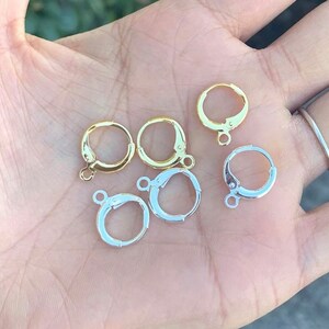 May include: Six earring hoops, three gold and three silver, with a hinged closure. The hoops are displayed on a hand.