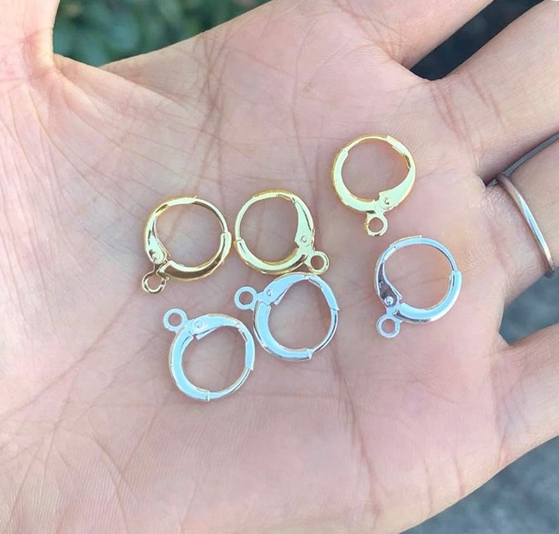 May include: Six earring hoops, three gold and three silver, with a hinged closure. The hoops are displayed on a hand.