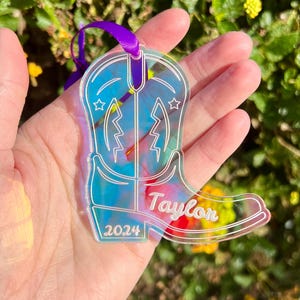 May include: A clear iridescent plastic cowboy boot ornament with the name "Taylor" and the year "2024" engraved on it.