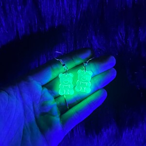 May include: A pair of green gummy bear shaped earrings. The earrings are made of clear plastic and glow in the dark.