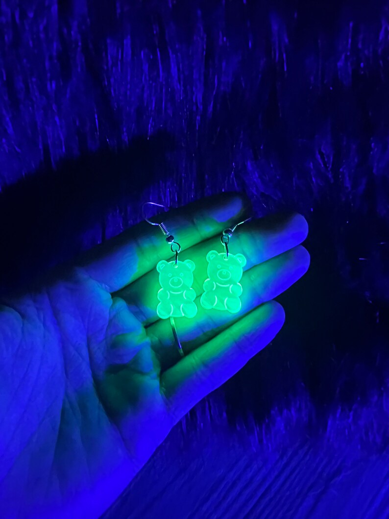 May include: A pair of green gummy bear shaped earrings. The earrings are made of clear plastic and glow in the dark.