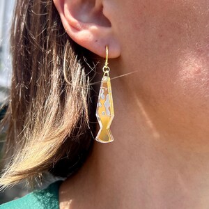 Op de afbeelding: Goudkleurige lava lamp oorbellen met een geel en wit ontwerp. De oorbellen hangen aan een gouden oorring. Een leuk en uniek accessoire.