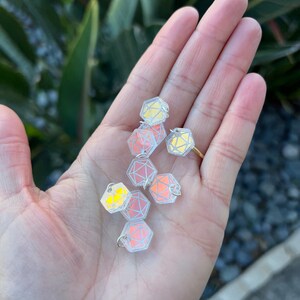 May include: A hand holding a group of iridescent, clear plastic, geometric shapes with silver rings. The shapes are reminiscent of dice.